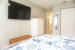 Ein Schlafzimmer mit einem Bett, einer Kommode, einem an der Wand befestigten Fernseher und einer Tür zu einem anderen Raum.