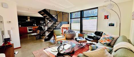 A modern living room with a staircase, a dining area, and large windows.