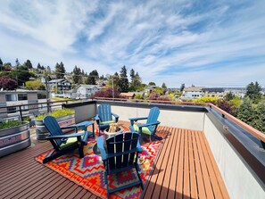 A rooftop deck with blue Adirondack chairs, a fire pit, and a colorful rug. - Magnolia Salmon Bay Calling · Rooftop Views (Seattle)
