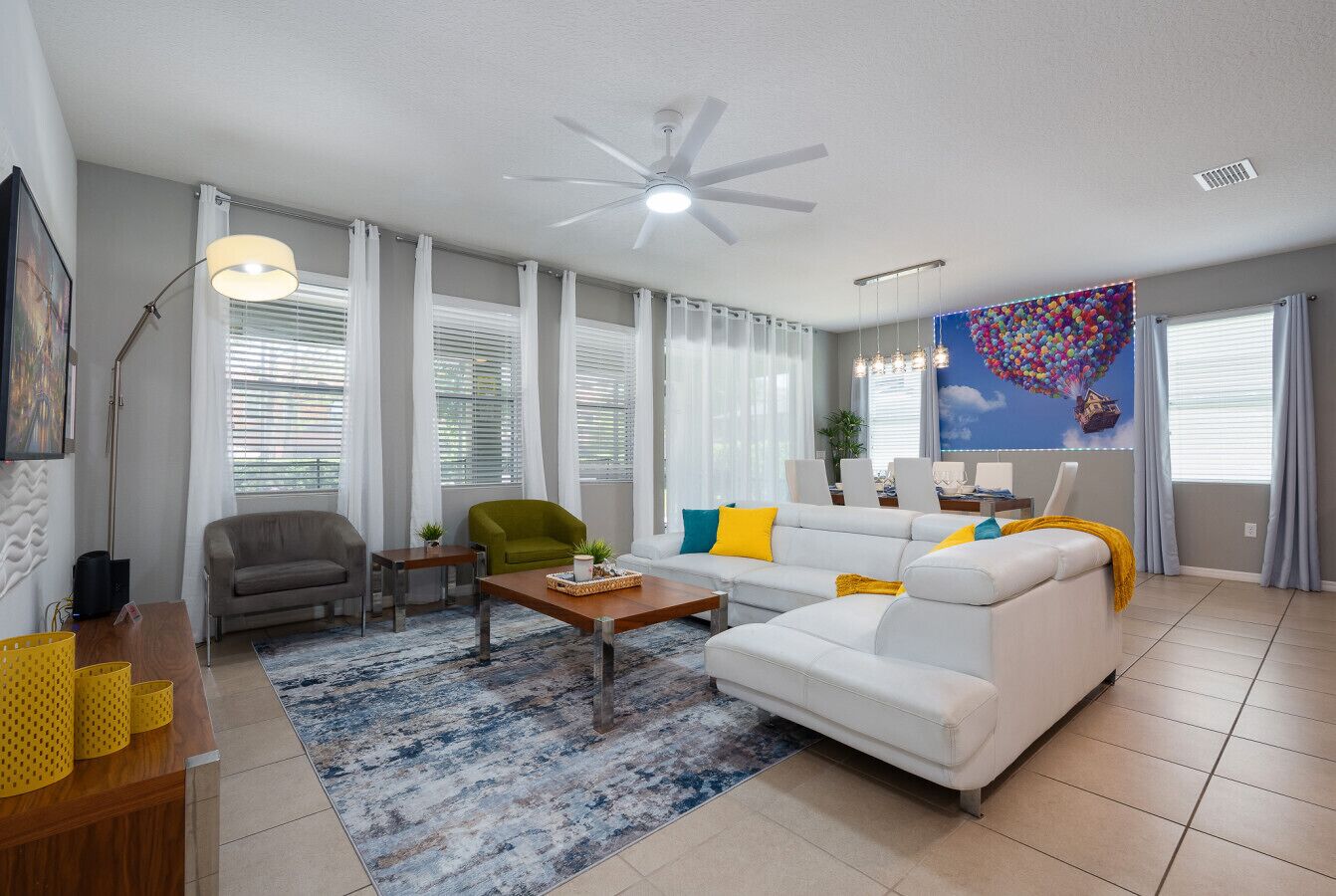 A living room with a ceiling fan, a white sofa, a green armchair, a coffee table, and a painting of balloons.