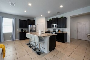 A modern kitchen with dark cabinets, a central island with bar stools, a refrigerator, microwave, stove, and a sink. - Sunset Swims & Disney Dreams-Modern Family Oasis (Davenport)