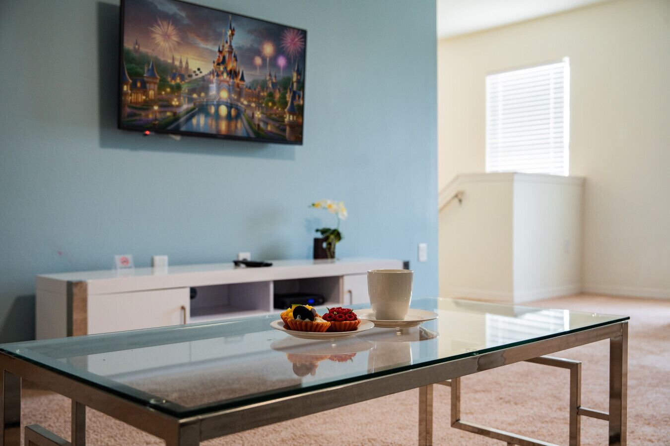 Una habitación con una mesa de vidrio, un armario blanco y un cuadro de un castillo en la pared.