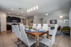 A modern kitchen with dark cabinets, a microwave, and a dining area with a wooden table and white chairs. - Sunset Swims & Disney Dreams-Modern Family Oasis (Davenport)