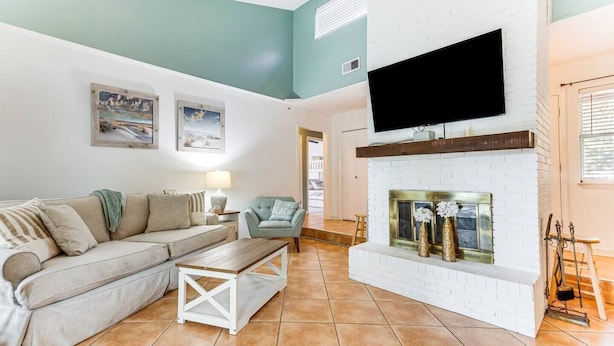 A living room with a white brick fireplace, a sofa, a coffee table, and a television mounted on the wall. - Pet-Friendly Family Getaway Near Two Beaches (Gulf Breeze)