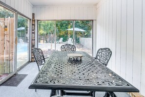 Eine Terrasse mit einem Metalltisch und -stühlen, einem Holzzaun und Blick auf einen Garten mit Rasen und Bäumen.