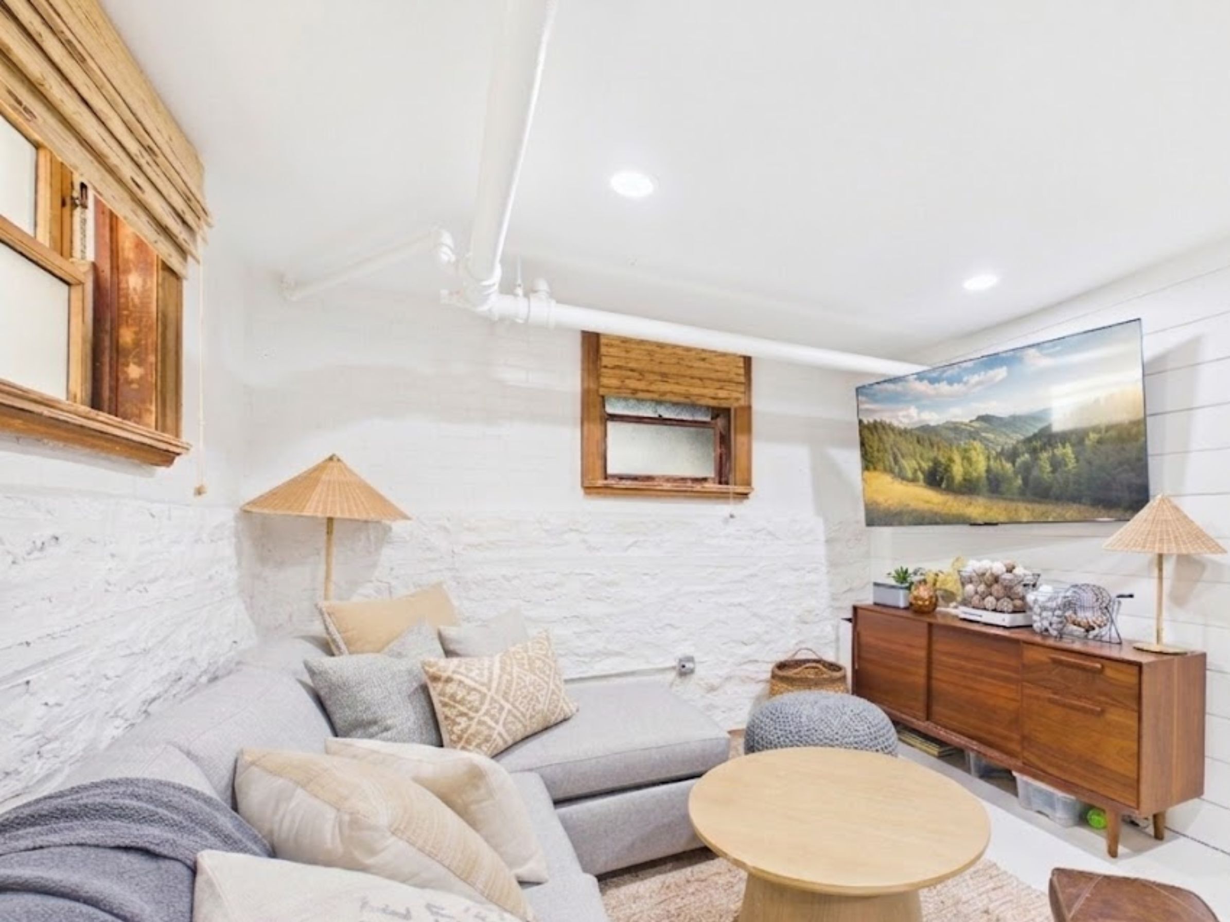 A modern living room with a white brick wall, a large flat-screen TV, a wooden cabinet, and a round wooden coffee table.