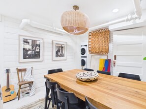 Ein Essbereich mit Holztisch, Stühlen, einer hängenden gewebten Leuchte und gerahmten Bildern an der Wand.
