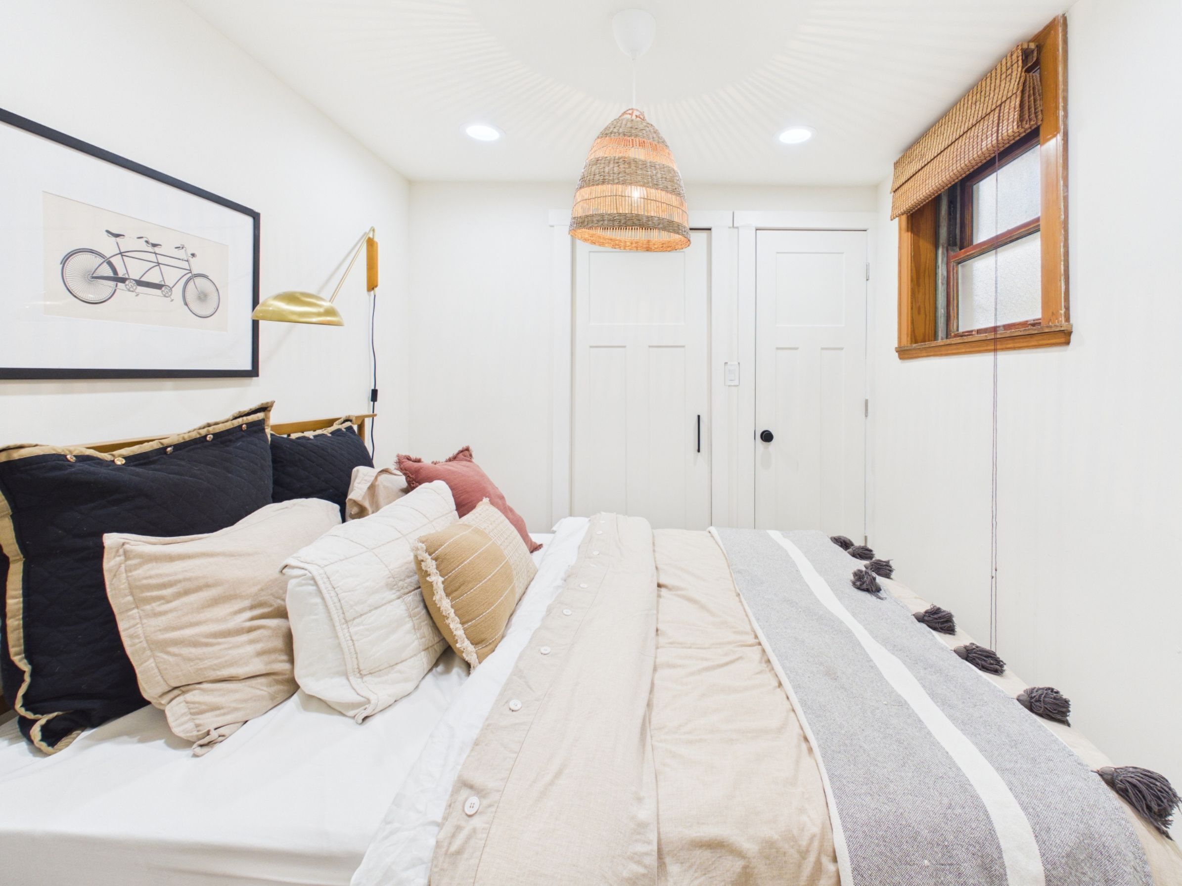 Une chambre avec un lit, une illustration de vélo sur le mur, un luminaire suspendu et une fenêtre avec un store en bois.