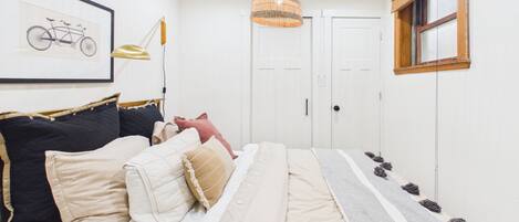 Une chambre avec un lit, une illustration de vélo sur le mur, un luminaire suspendu et une fenêtre avec un store en bois.
