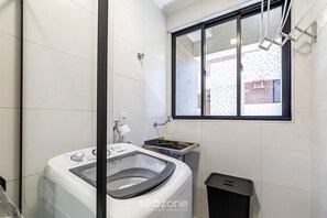 Ein kleiner Hauswirtschaftsraum mit Waschmaschine, Spüle und Mülleimer.