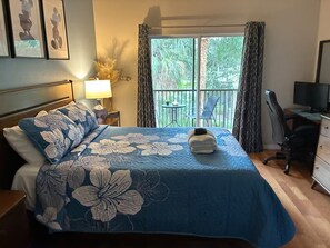 Ein Hotelzimmer mit Bett, Schreibtisch, Stuhl, Lampe und einem Balkon mit Blick auf Bäume.