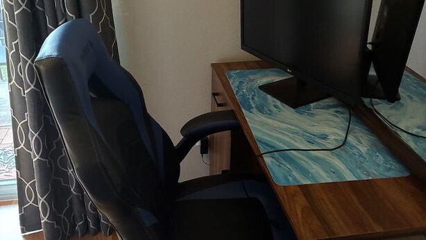 A room with a wooden desk, two monitors, a black office chair, and patterned curtains. - Sunshine Vacation Retreat: Spacious 3-bedroom condo in serene Kissimmee with AC (Kissimmee)