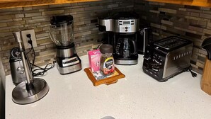 A kitchen with wooden cabinets, a coffee maker, a toaster, a blender, and a coffee pod holder. - Sunshine Vacation Retreat: Spacious 3-bedroom condo in serene Kissimmee with AC (Kissimmee)