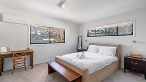 Ein Schlafzimmer mit einem Bett, einem Schreibtisch, einem Stuhl, einem Nachttisch und einem Fenster mit Blick auf Bäume.