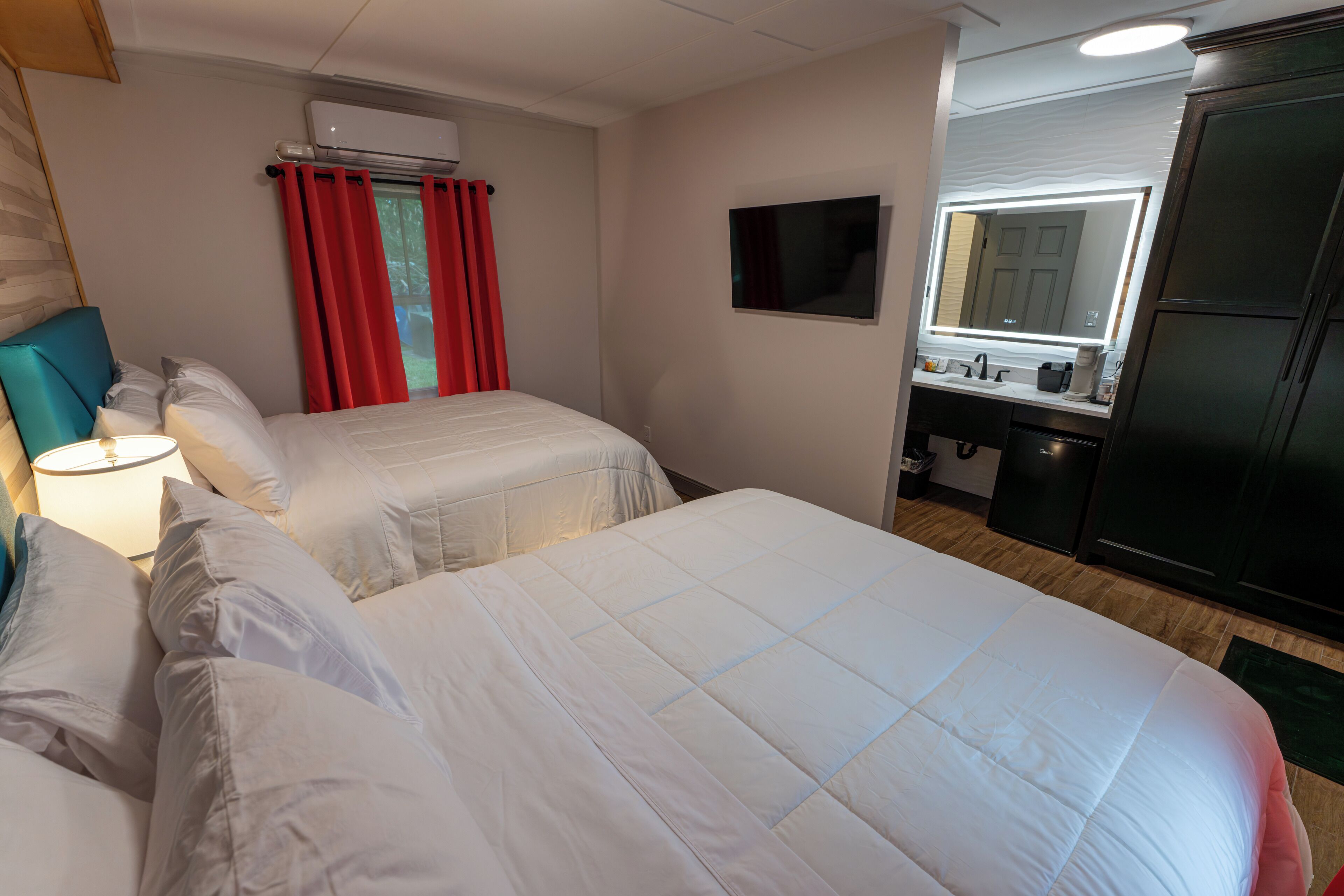 Een hotelkamer met twee bedden, een televisie, een minibar en een badkamer met een spiegel.