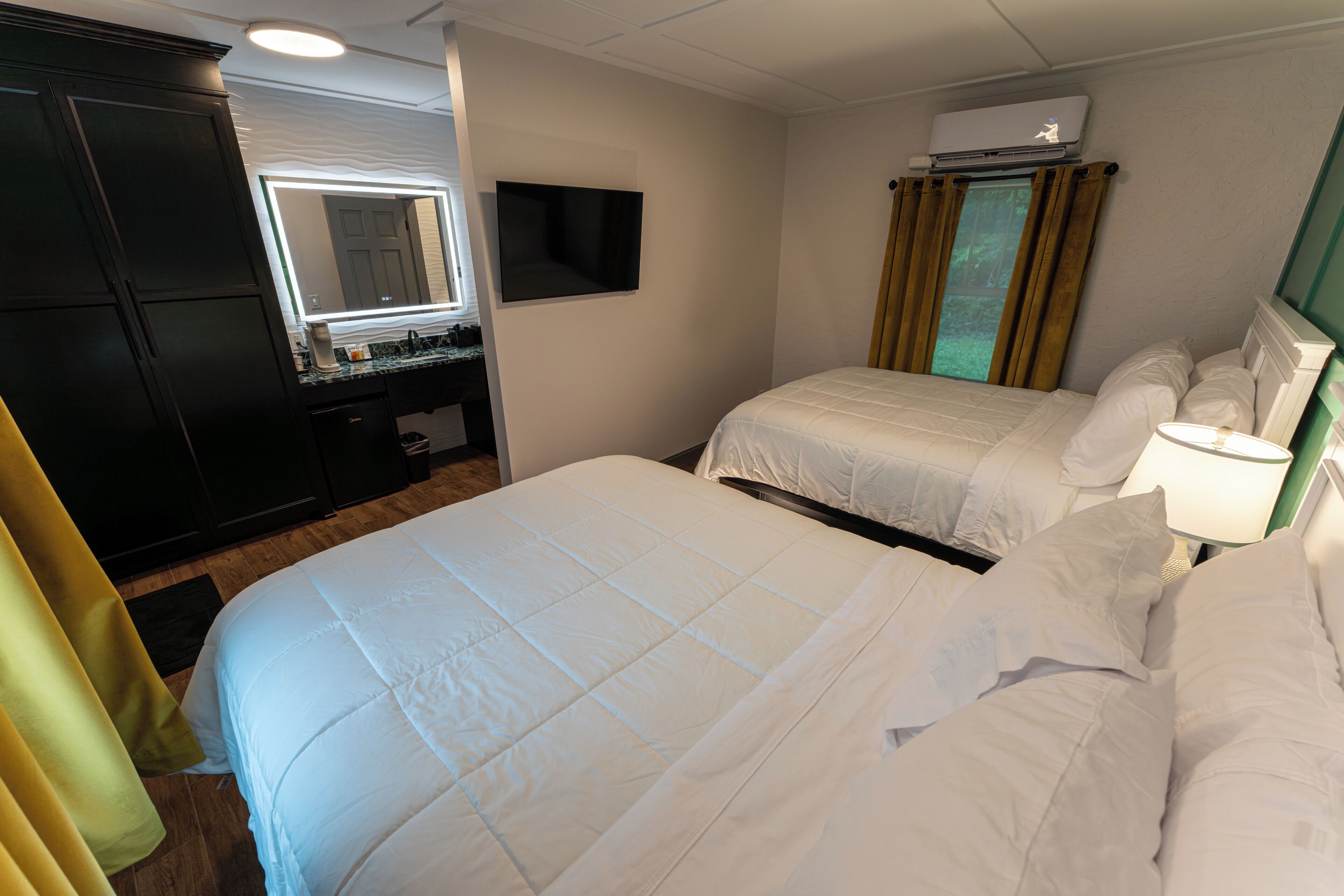 Habitación de hotel con una cama grande, una mesita de noche, un televisor montado en la pared y una ventana con cortinas.