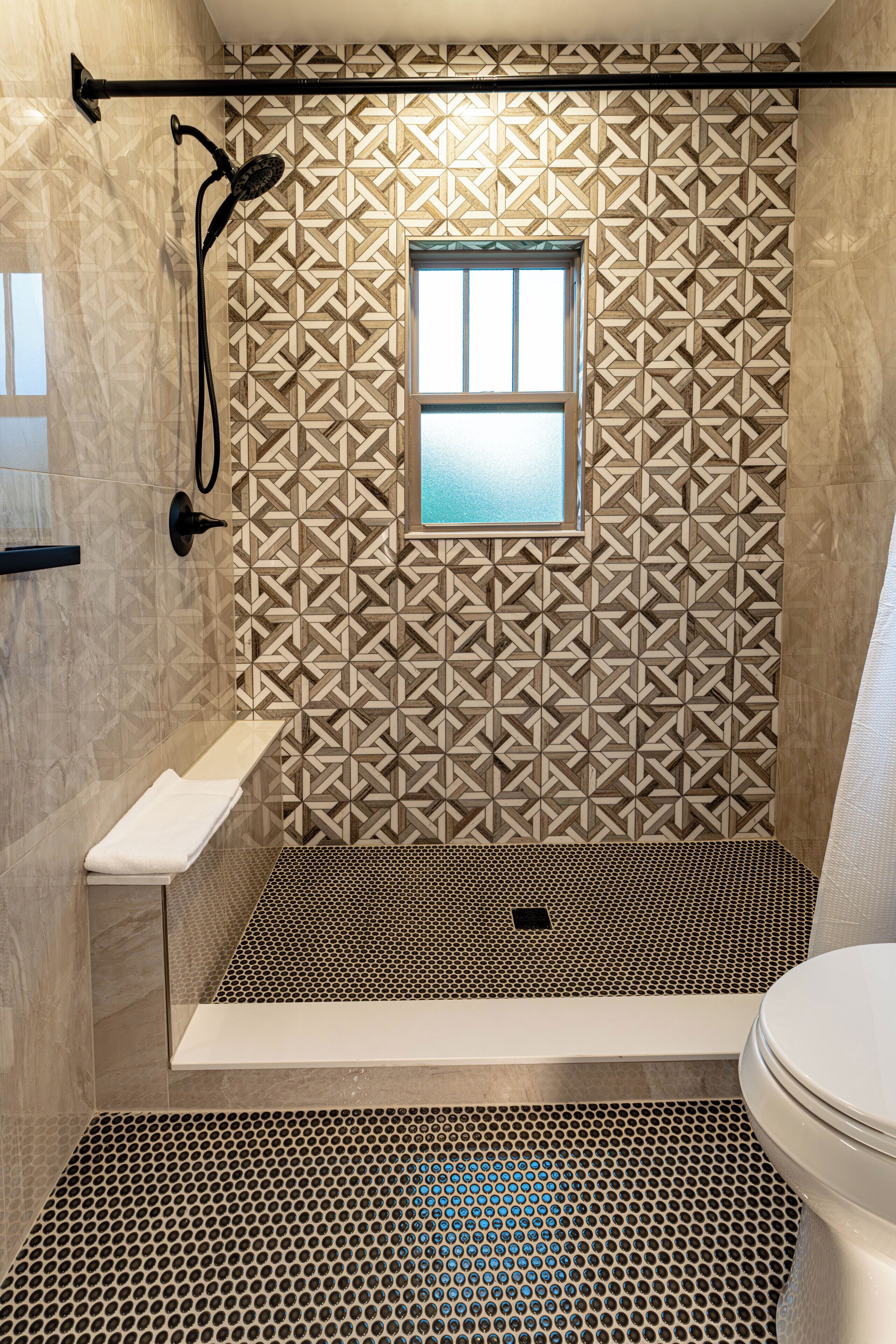 A bathroom with a geometric patterned wall, a window, a shower, a sink, and a toilet.
