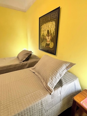 Una habitación con dos camas, un cuadro en la pared y una pequeña mesa de madera.