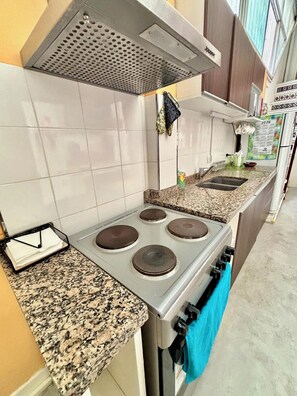 Una cocina con estufa a gas, cuatro quemadores, extractor y encimera de granito.