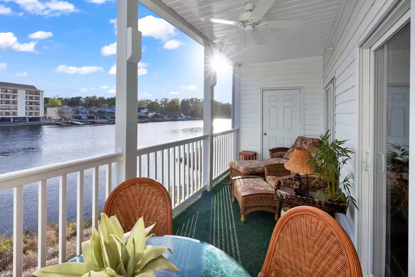 Een overdekt terras met rieten meubels, een tafel en een potplant.