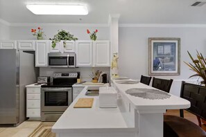 A modern kitchen with white cabinetry, stainless steel appliances, a central island, and a dining area with a table and chairs. - 2BR 2Bath Intracoastal waterfront condo in golf course community Dog friendly!  (Myrtle Beach)
