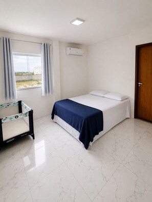 Une chambre à coucher avec un lit, une fenêtre avec des rideaux, un appareil de climatisation et une porte.