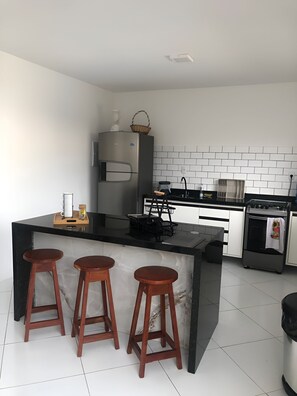 A modern kitchen with a central island, bar stools, a refrigerator, a stove, and a microwave.