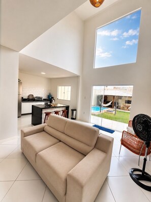 A modern living room with a sofa, a dining area with a table and chairs, and a view of a swimming pool and outdoor space.