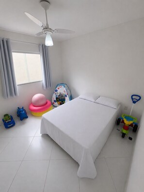 A bedroom with a bed, a ceiling fan, a window with curtains, and children's toys.