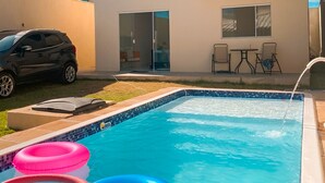 A swimming pool with three inflatable rings, a car parked outside, and a building with a sliding door. - Beach house in Jacuípe | Bahia coast | 4 bedrooms | Pool and gourmet area (Camaçari)