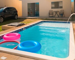 A swimming pool with three inflatable rings, a car parked outside, and a building with a sliding door. - Beach house in Jacuípe | Bahia coast | 4 bedrooms | Pool and gourmet area (Camaçari)