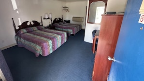 Habitación de hotel con dos camas, un escritorio, una silla, un espejo y un armario.