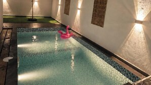 Una piscina con un flotador de flamenco rosa, rodeada de muros con diseños texturizados y luces empotradas.