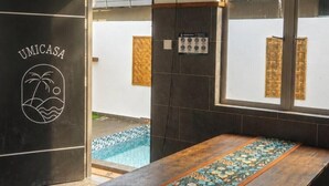 Una habitación con una mesa larga, un banco y una piscina visible a través de la puerta.