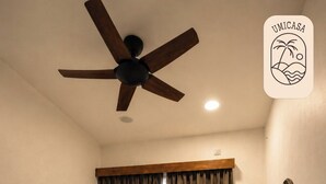 Un dormitorio con cama, ventilador de techo, televisor montado en la pared y ventana con cortinas.