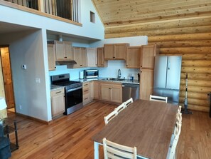 A modern kitchen with wooden cabinets, a central island, stainless steel appliances, and a dining area.