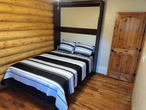 A single bed with a striped bedspread and two pillows, a wooden door, and a wooden wall.