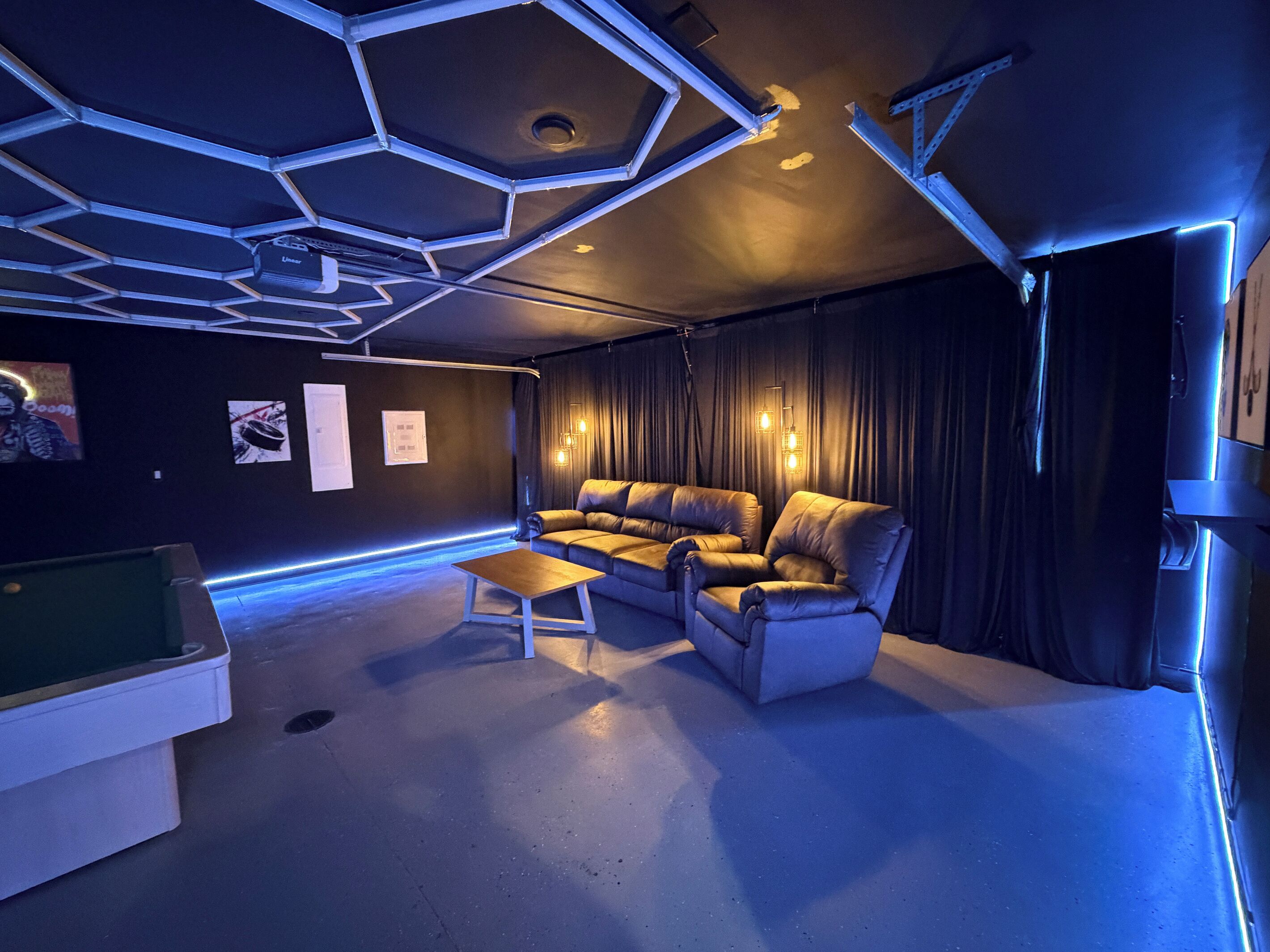 A modern room with a hexagonal ceiling, a leather sofa, a small coffee table, and a pool table.