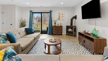 Una sala de estar con sofá, mesa de centro, chimenea, televisor y vista a través del ventanal.