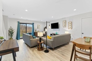 Ein modernes Wohnzimmer mit einer Couch, einem Esstisch und einem an der Wand montierten Fernseher.