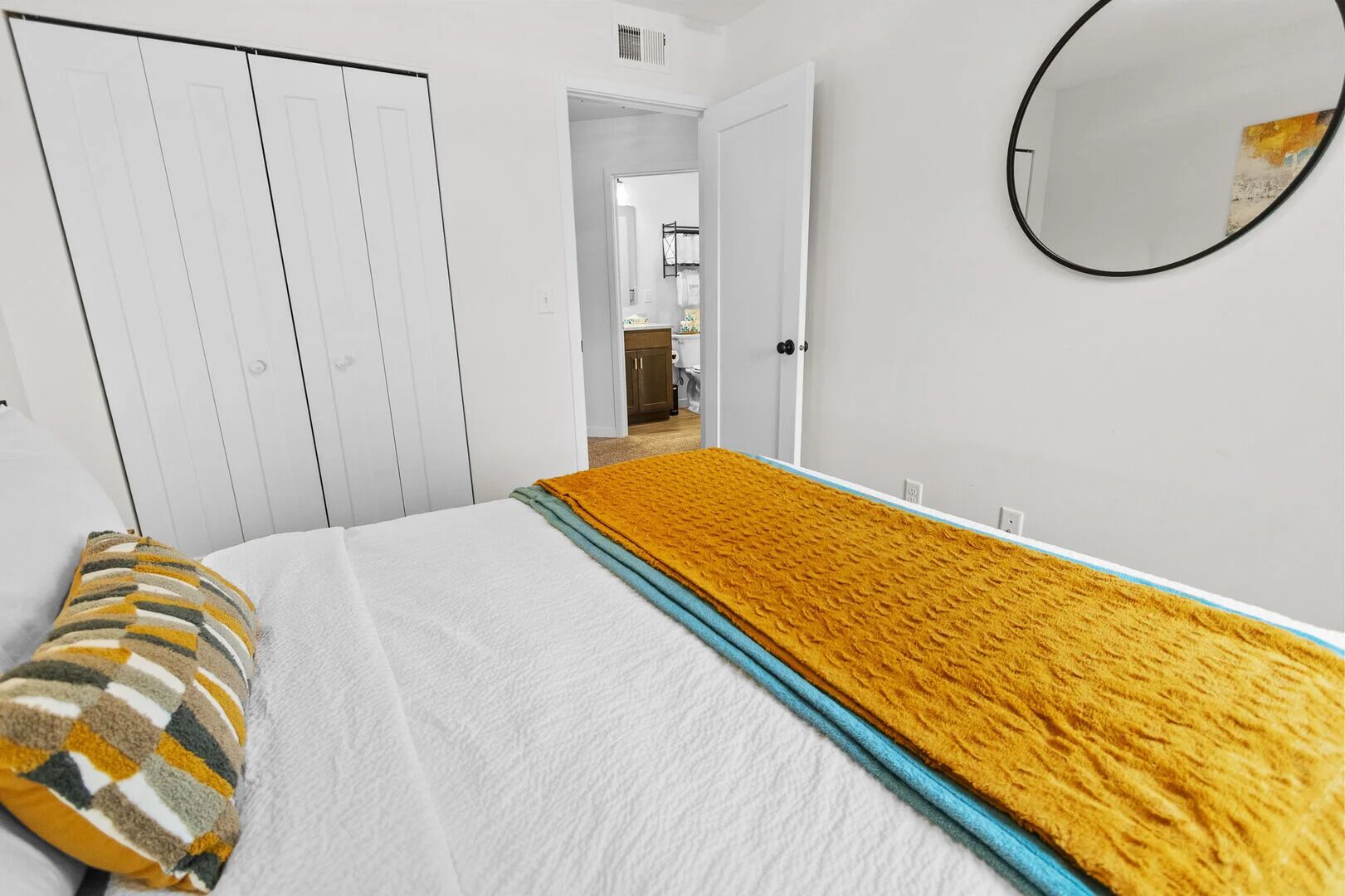 Un dormitorio con cama, armario, espejo y un pasillo que lleva a un baño.