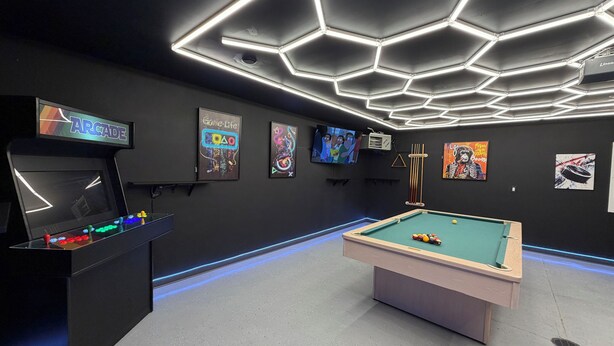Una habitació amb billar, jocs arcade i obres d'art a les parets.