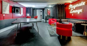 A ping pong table, red chairs, a sofa, and a neon sign reading 'Playmate Lounge'. - The Playmate - a Glam Rooftop Retreat with Hot Tub, Putting Green & Skyline View (Nashville)