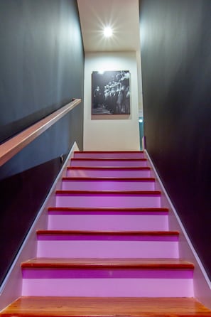 Un escalier aux marches violettes mène à une pièce dont un mur est sombre et sur lequel est accroché un tableau encadré.