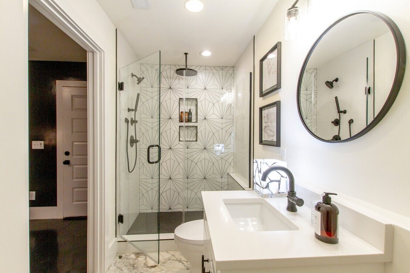 A modern bathroom with a glass-enclosed shower, a white sink, a large mirror, and a marble floor.