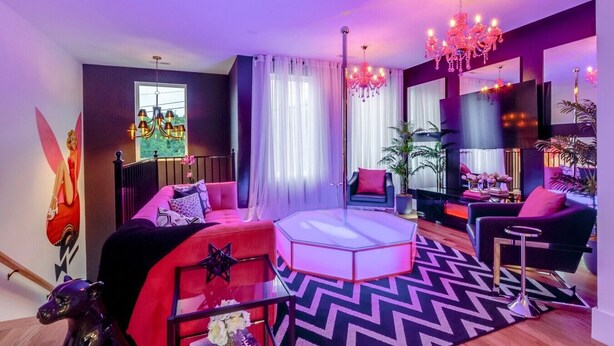 A modern living room with a red sofa, a round white ottoman, a black and white chevron rug, and a large mirror. - Playmate Lounge - Glam Rooftop Retreat | Hot Tub, Putting Green & Skyline Views (Nashville)
