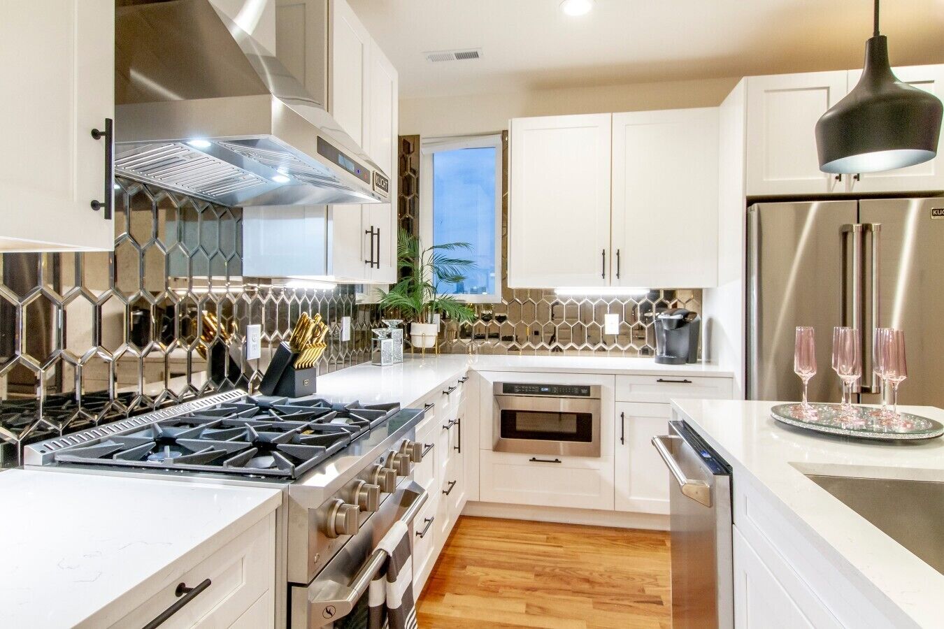A modern kitchen with stainless steel appliances, white cabinetry, and a hexagonal backsplash.