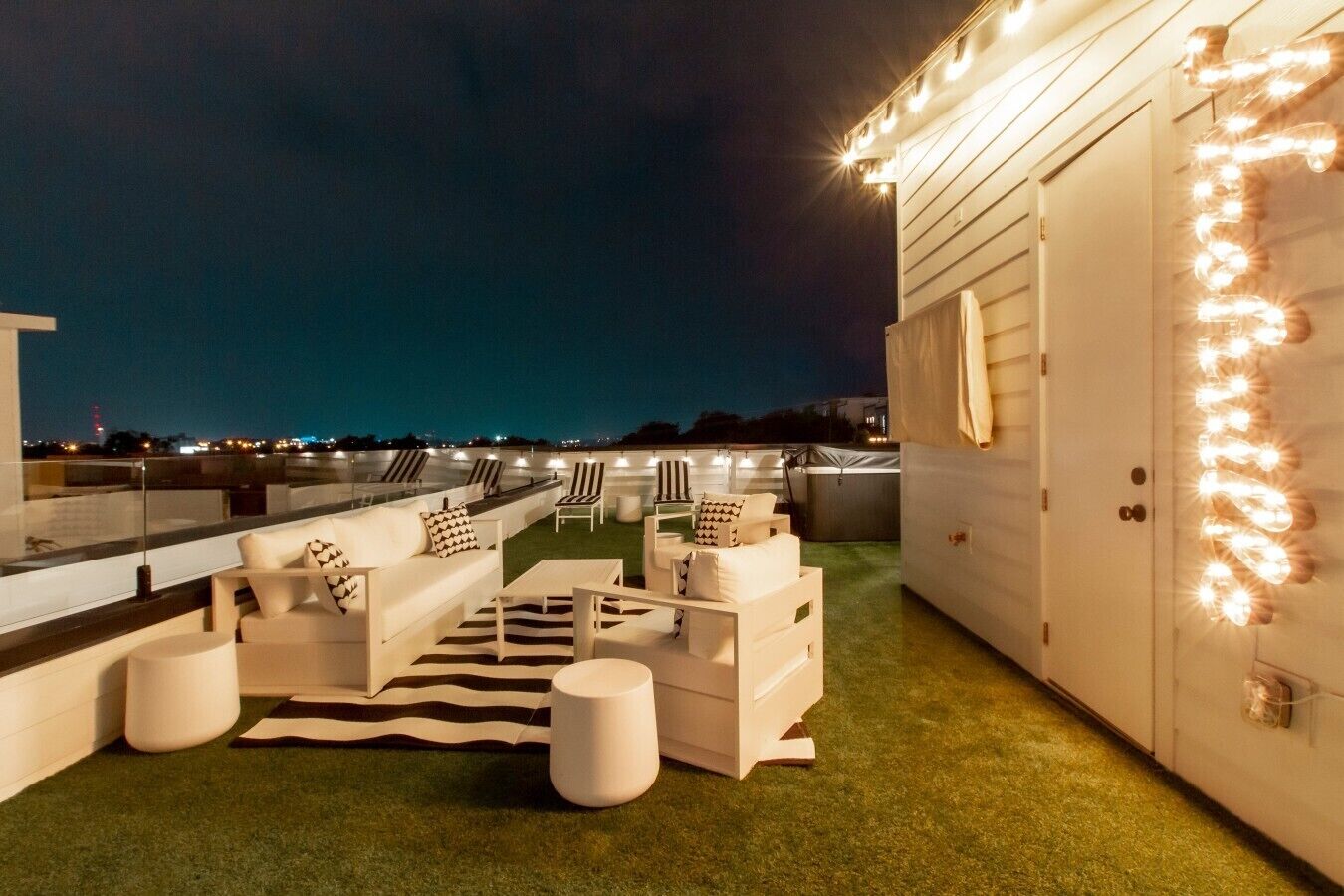 A rooftop terrace with outdoor seating, a view of the cityscape, and string lights.