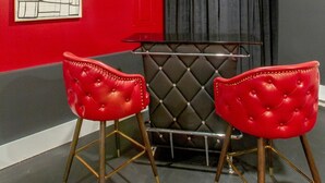 A room with a red wall, a black tufted chair, and a black cushioned bench. - Playmate Lounge - Glam Rooftop Retreat | Hot Tub, Putting Green & Skyline Views (Nashville)