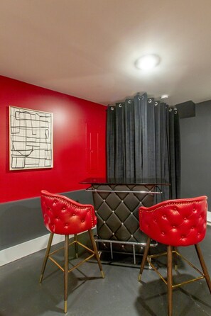 Um quarto com parede vermelha, cadeira estofada preta e um banco acolchoado preto.